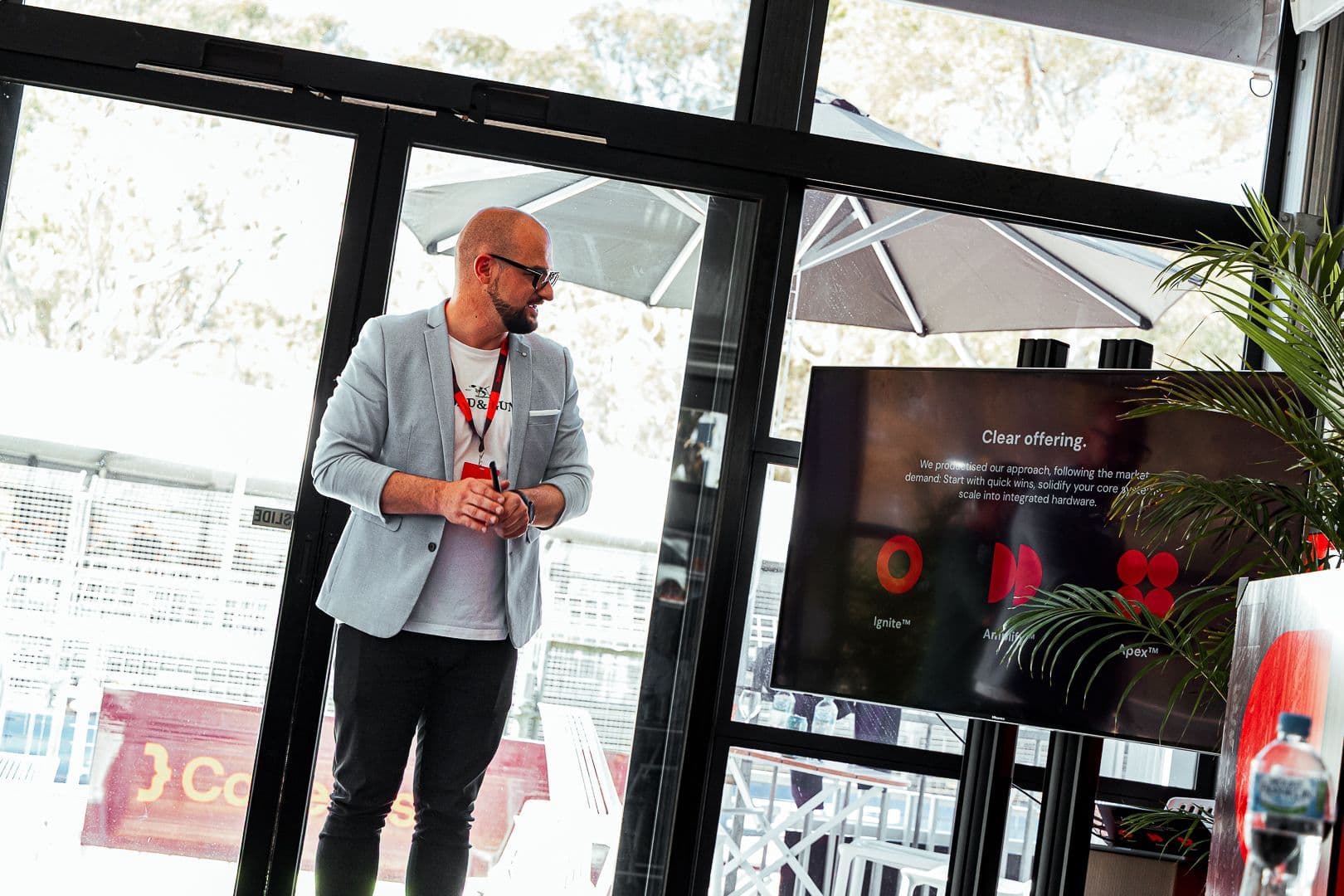 A presenter speaking beside a screen reading Clear offering in a branded marquee