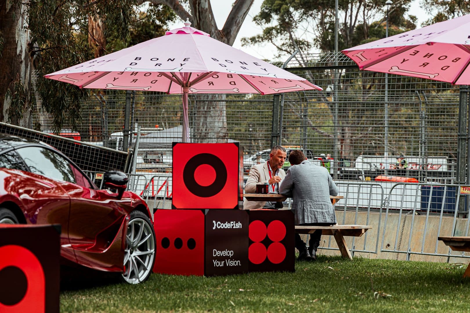 Guests seated at a picnic table beside CodeFish Develop Your Vision signage and a red sports car