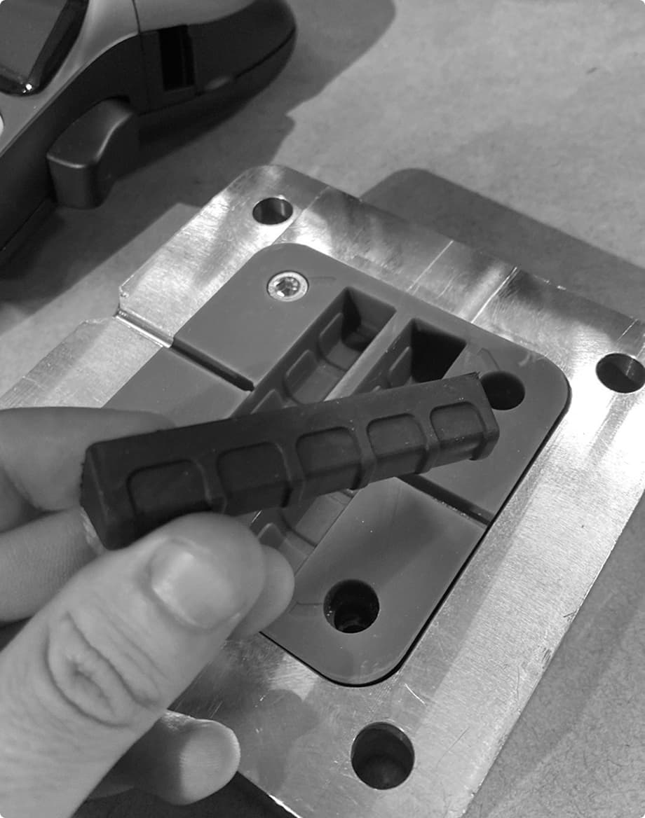 A hand holding a moulded rubber part beside its aluminium tooling block
