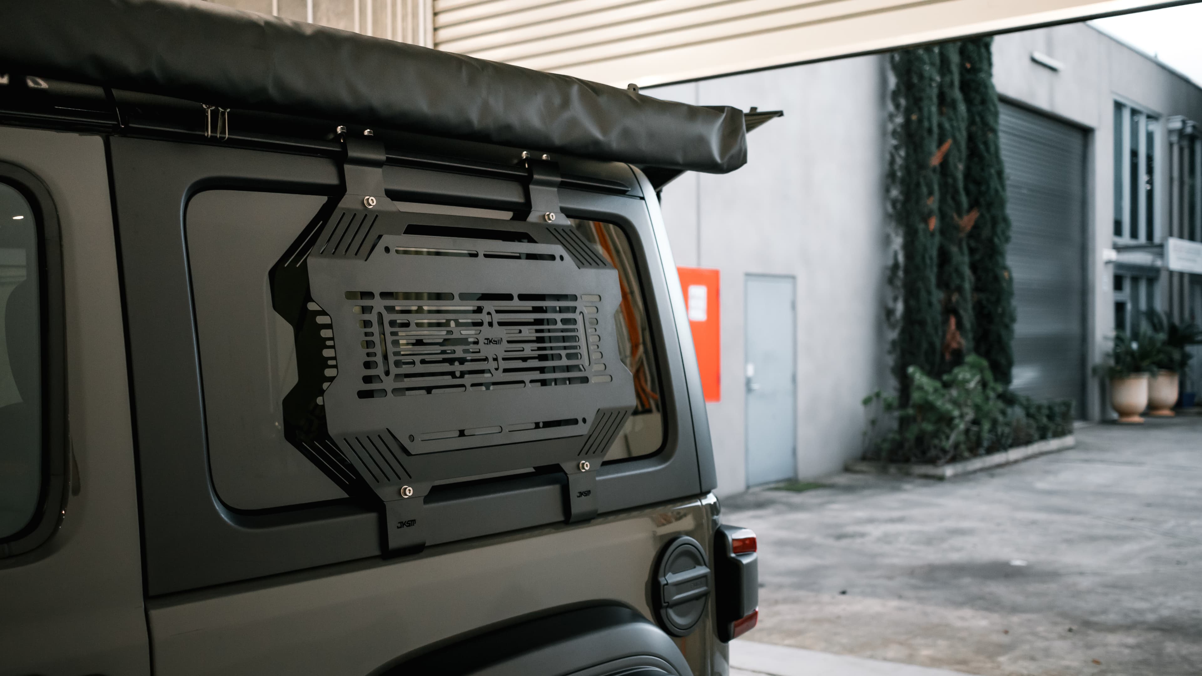 Raw alloy storage panel fitted to a four-wheel drive rear window outside an industrial workshop