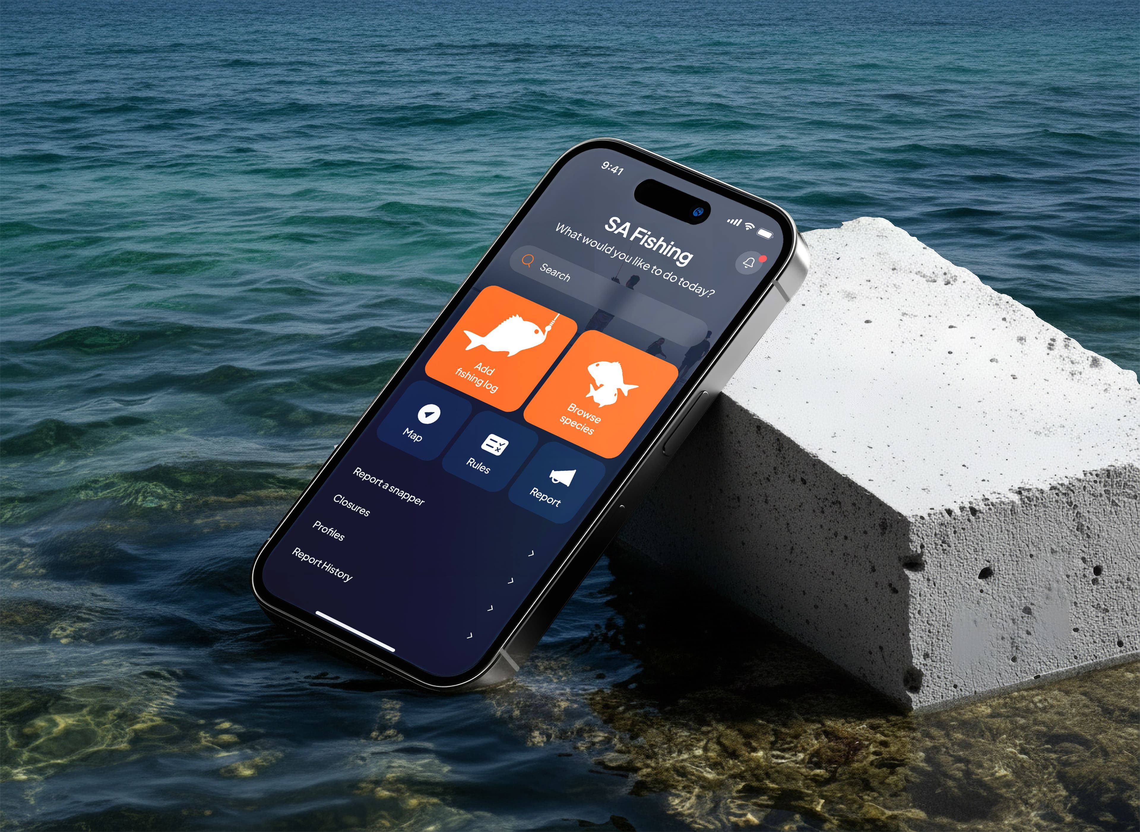 Phone resting on a concrete block in shallow sea water showing the SA Fishing app home screen