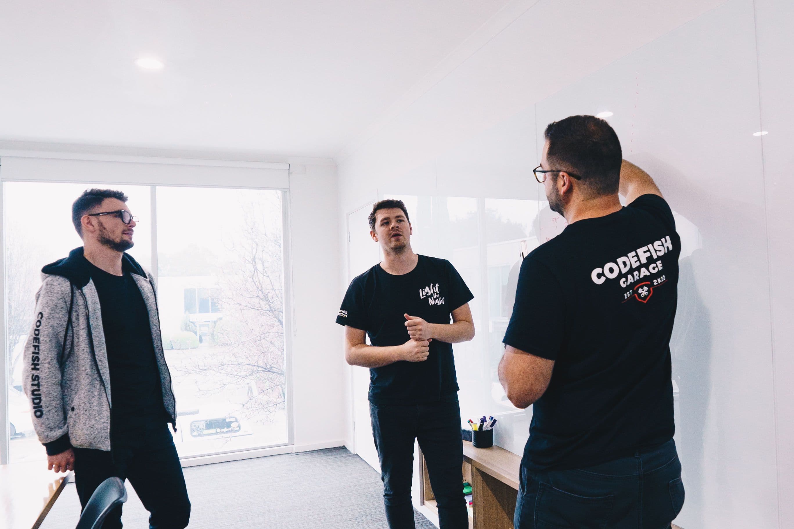 Three team members in CodeFish shirts talking in a whiteboard scoping session