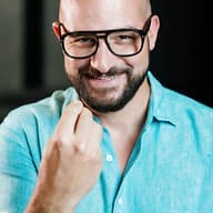 A smiling team member wearing glasses and a turquoise linen shirt